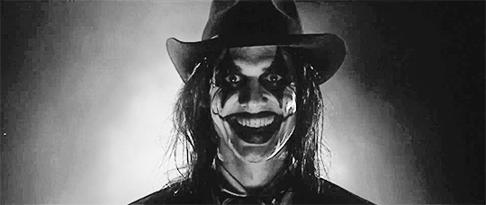 a selfie of me. i have wavy black hair, my makeup is done in a trad goth style, and i’m wearing a black leather jacket and red bodice-style top.